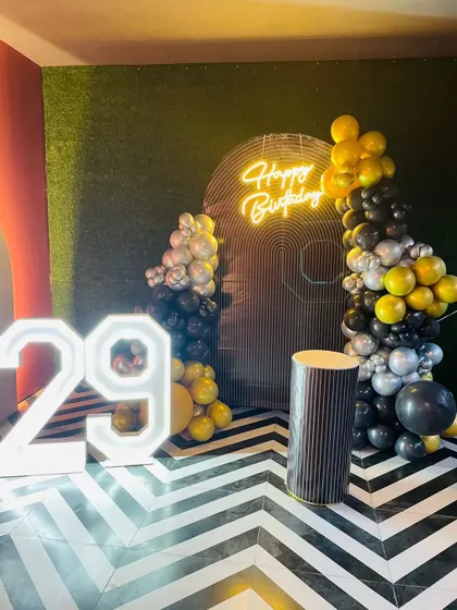 A modern 29th birthday setup with a black, silver, and yellow balloon arrangement against a geometric-patterned floor.