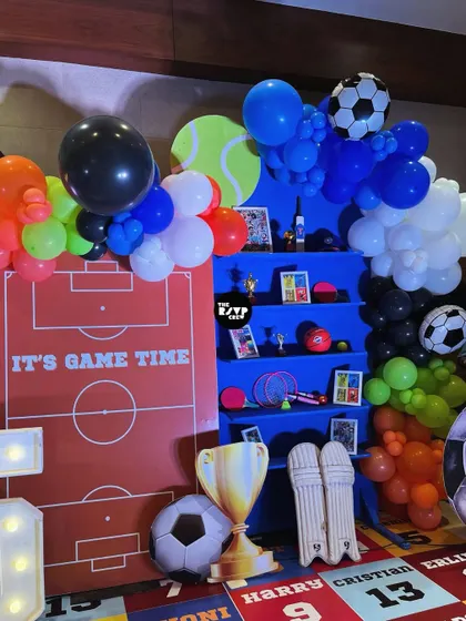 It's game time! This setup includes a soccer field backdrop, a shelf filled with sports equipment, and plenty of soccer ball balloons.