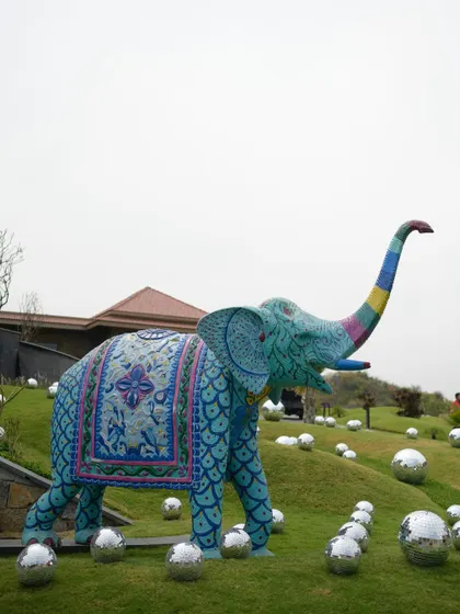 A quirky, painted elephant statue surrounded by disco balls on a grassy knoll, a perfect example of blending tradition with fun.