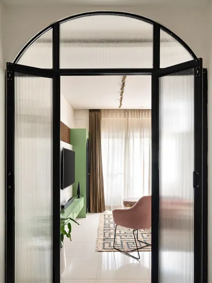 I used a metal and fluted glass partition with a bold arch to create a dramatic entryway into the living room. It separates the space while allowing light to pass through, offering a tantalizing glimpse of the colorful interior.