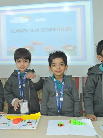 A group of proud students stands behind a table displaying their finished clay models, showcasing the variety of their creations.