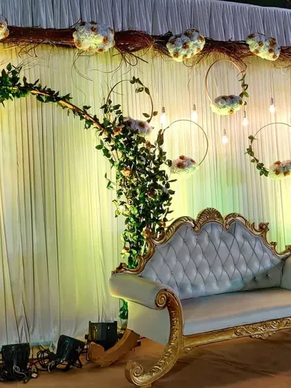 This reception stage combines rustic and romantic elements. A graceful arch of greenery and flowers frames the couple's seating, with hanging floral hoops and lights adding a touch of whimsy.