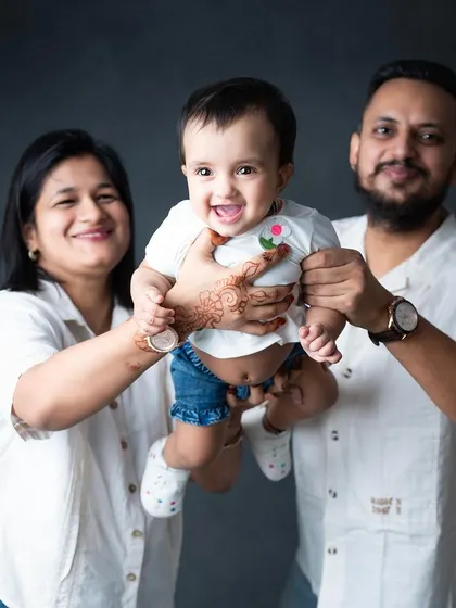 A happy family of three, holding their baby girl up for the camera with big smiles.