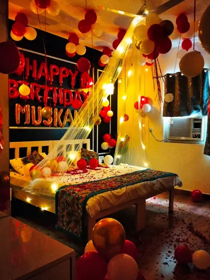A full view of a romantic bedroom decoration for "Muskan". The setup includes a canopy, fairy lights, and a mix of red, white, and gold balloons.