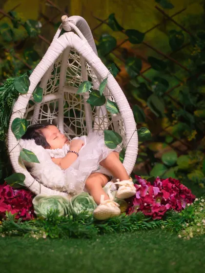 Sleeping soundly in a garden swing. This whimsical setup uses a hanging chair, lush greenery, and flowers to create an enchanted garden feel for a newborn portrait.
