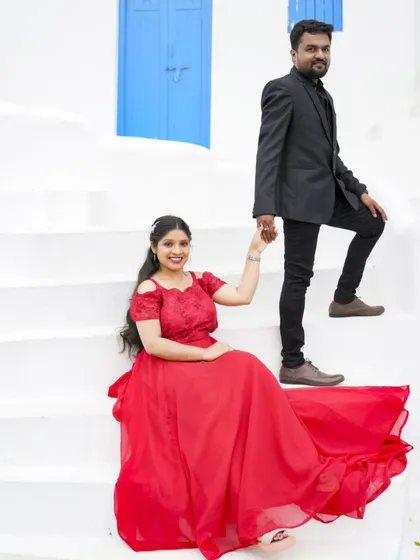 A classic pose on the steps of our Santorini-themed location. The bride's red gown and the groom's holding her hand create a timeless romantic photo.