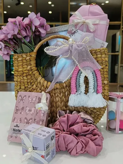 The pink self-care hamper unboxed, showing the butterfly-themed notebook, macrame rainbow keychain, and oversized scrunchie.