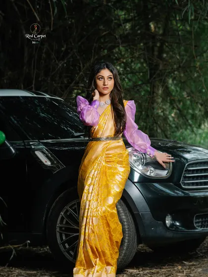A high-fashion shot of Sanjana Rao posing next to a car. The contrast between the traditional saree and the modern setting is striking.
