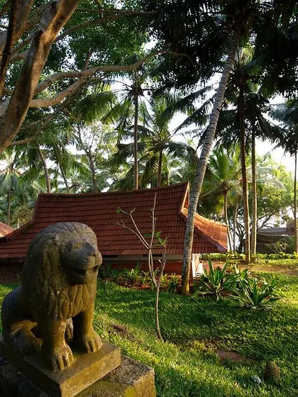 A stone lion sculpture stands guard in the lush gardens of the Niramaaya Resort. The landscape design incorporates traditional elements and native plants to create an authentic and serene atmosphere.