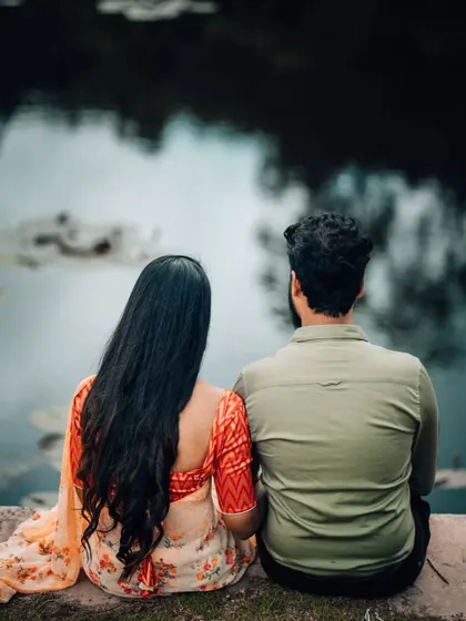 A quiet moment of reflection for a couple sitting by a lake, captured from behind to create a sense of shared intimacy.