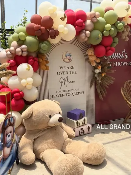 A close-up of the baby shower photo corner, featuring a large teddy bear, a custom backdrop, and a beautiful balloon arch with pampas grass details.