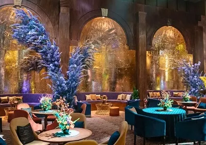 The main lounge area of the club-themed Sangeet, with curved seating, bold blue floral arrangements, and textured gold alcoves.