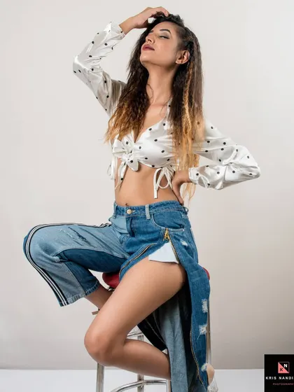 A dynamic pose from the 'Polka Dots' series. The model is seated on a stool, showing off the edgy, unzipped jeans and her confident, carefree attitude.