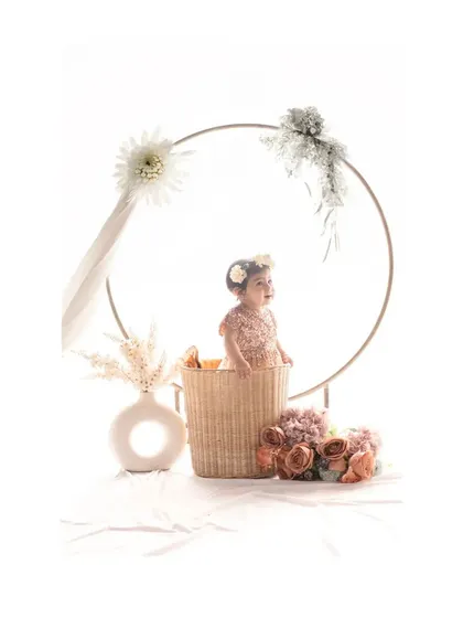 In this variation, the baby looks to the side, creating a candid and sweet profile shot within the beautifully arranged floral hoop setup. The soft lighting enhances the gentle and dreamy feel of the portrait.