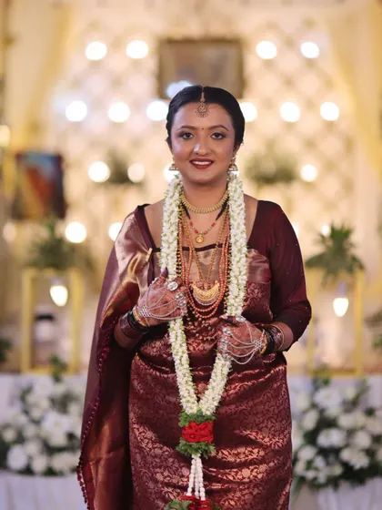 A portrait of a Coorgi bride with her garland. Her makeup is soft and elegant, with a deep red lip that complements her maroon saree.