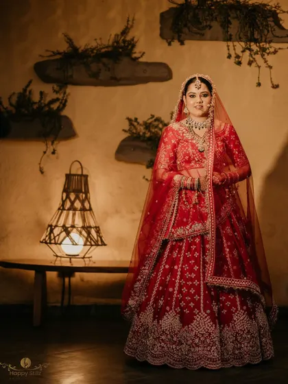 A beautiful full-length portrait of the bride in her red wedding lehenga, standing in a warmly lit, rustic-chic room.