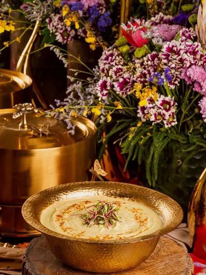 A beautifully presented main course from our Modern Indian catering menu, served in elegant brassware amidst lush floral arrangements for a designer party.