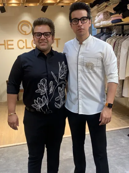 My brother Nikhil and I, the founders of The Closet. We are wearing two of our custom shirt designs, a black floral embroidered shirt and a white asymmetrical zip shirt, showcasing our unique approach to smart casual wear.