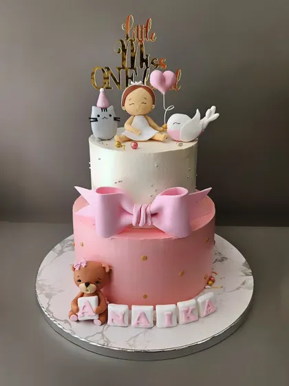A cake that is just "Ati Sundar". This two-tier cake for Naika's first birthday is pure elegance, with a big pink bow, a teddy bear, and a cute figurine with her animal friends.