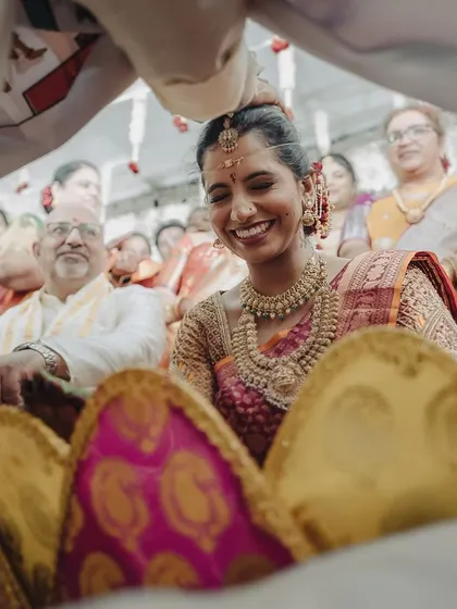 The bride’s joyful expression as she peeks from under the traditional Terasala cloth during the Jeerige Bella ritual. It's a classic, candid moment in a South Indian wedding, full of anticipation and happiness.