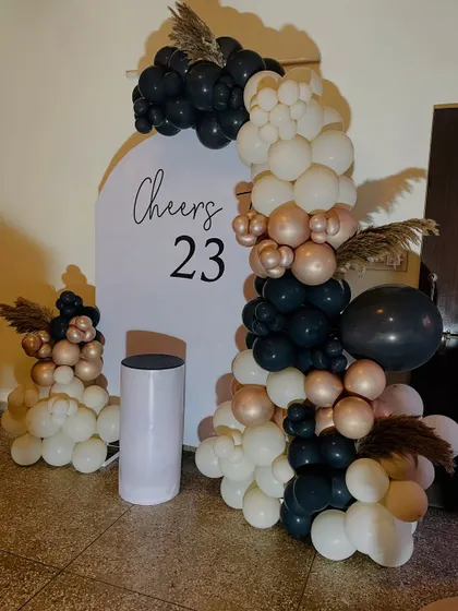 A stylish "Cheers to 23" birthday setup with a modern balloon arch in black, white, and rose gold.