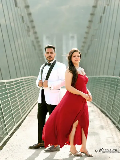 A stylish couple poses on a modern suspension bridge in Rishikesh. The contrast between their formal wear and the rugged natural landscape creates a striking visual.