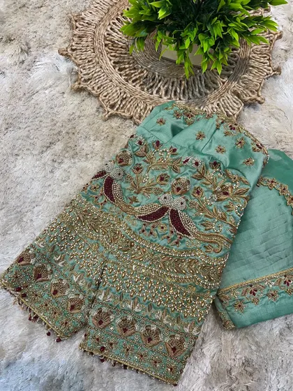 This pastel green blouse features exquisite embroidery with peacock motifs, highlighted with maroon and gold thread. It's a piece of wearable art.