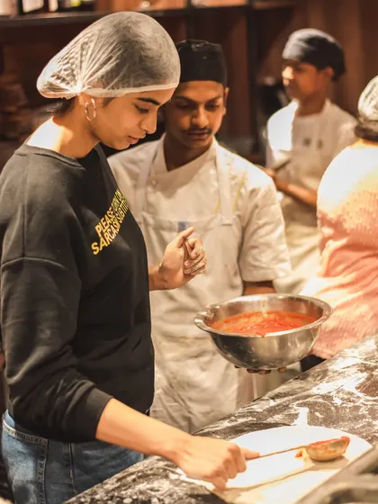 One of our chefs guides a guest as she spreads the San Marzano tomato sauce on her dough. We're there to help you make the perfect pie.