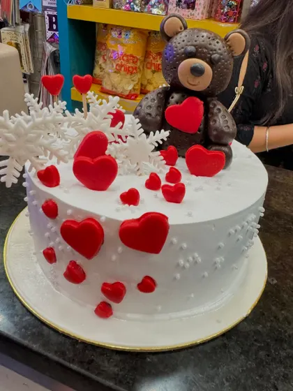 A custom cake for a husband, featuring a chocolate teddy bear holding a heart. The design is filled with love, with fondant hearts and snowflake details, making it a sweet and personal gift.