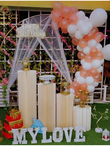 A romantic birthday setup with a peach and white balloon arch and 'MY LOVE' marquee letters.