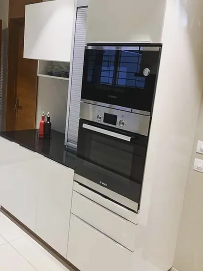 A view of the tall unit in the Lajpat Nagar kitchen, featuring a built-in oven and microwave. The glossy white finish of the unit contrasts nicely with the adjacent black countertop.