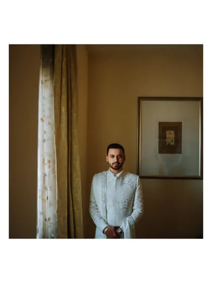 A classic portrait of the groom standing by a window, using natural light for a timeless feel.