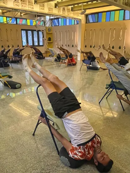 A room full of athletes in a supported Viparita Karani (Legs-up-the-Wall Pose) variation using chairs. This is a primary recovery pose, helping to drain fluid from the legs and calm the nervous system.