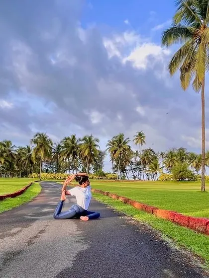 Practicing Eka Pada Rajakapotasana on a path surrounded by palm trees. Yoga is a light which, once lit, will never dim. The better your practice, the brighter your flame.