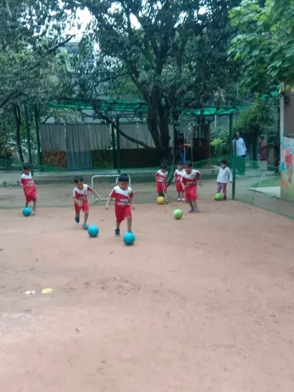 A group of toddlers in their red uniforms, dribbling their balls in a sandy play area.
