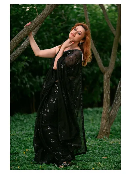 An elegant outdoor portrait in a black sequined saree. The natural setting provides a beautiful contrast to the glamorous attire.