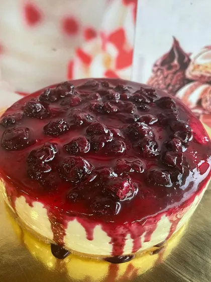 A full view of our eggless Blueberry Cheesecake, showcasing the glossy, fruit-packed blueberry compote dripping down the sides of the creamy cake.
