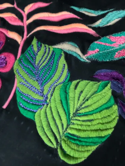 A detail of colorful, tropical leaves rendered in vibrant embroidery. Each stitch resonates with nature's beauty, woven into a timeless design.