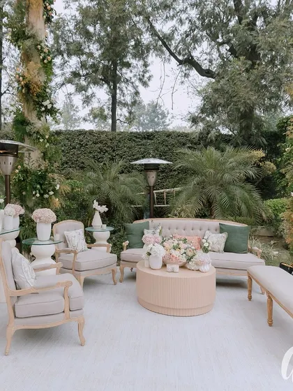 An outdoor lounge area designed with muted, earthy tones. The light-colored furniture and soft green cushions blend seamlessly with the surrounding garden environment.