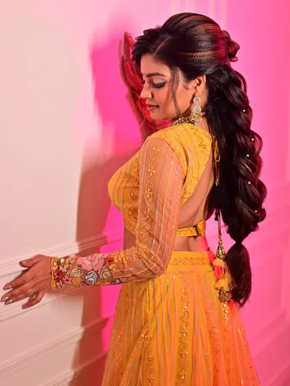 A view of the detailed hairstyle and backless blouse design. The makeup is kept flawless from all angles, with a focus on a clean profile and radiant skin that glows under the pink studio lighting.