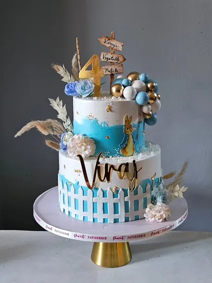Step into a whimsical world with this adorable Peter Rabbit-themed cake. This two-tier design for a 4th birthday features a picket fence, delicate florals, and a charming Peter Rabbit illustration.