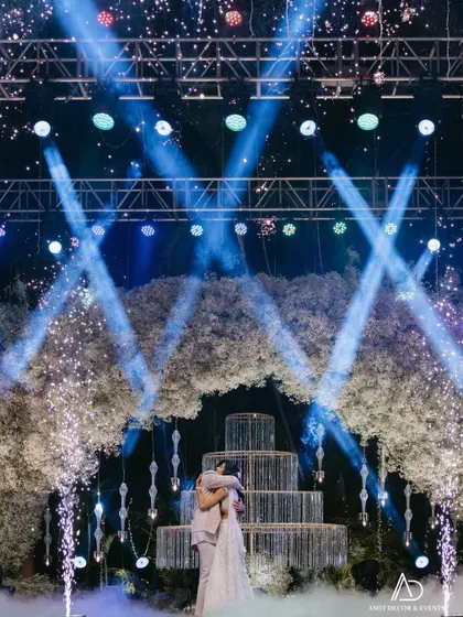 A romantic embrace under the floral arch, with dramatic blue spotlights and fireworks creating a magical, cinematic moment for the couple.