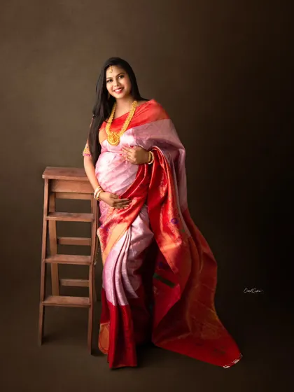 A classic portrait of a mom-to-be in a beautiful pink and red silk saree, accessorized with traditional gold jewelry.