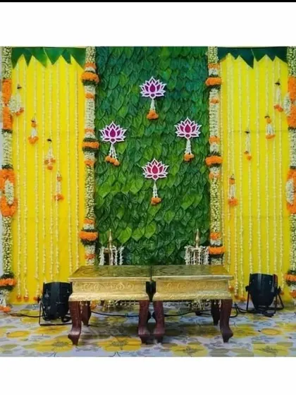 A Varamahalakshmi festival backdrop featuring a banana leaf wall, yellow flower hangings, and lotus cutouts.