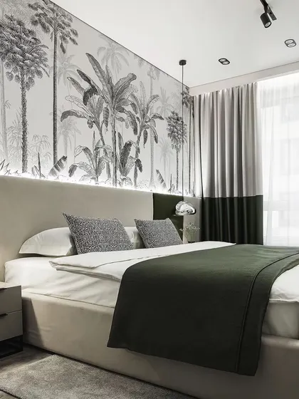 A bedroom with a striking black-and-white palm tree wallpaper, creating a bold, graphic feature wall. The green and grey bedding complements the design.