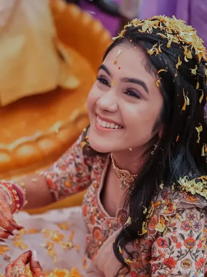 A beautiful, candid shot of the bride's happy smile during the Haldi ceremony, with flower petals in her hair.