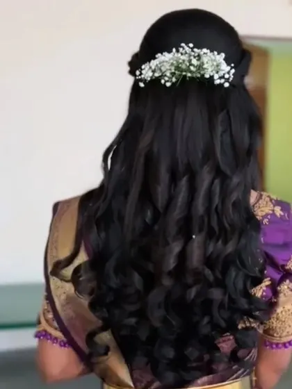 A half-up style with a simple braid and curls, finished with a sprig of baby's breath.
