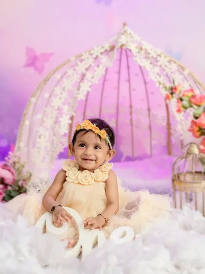 Holding the "One" sign, this little girl celebrates her first birthday in a magical butterfly garden.