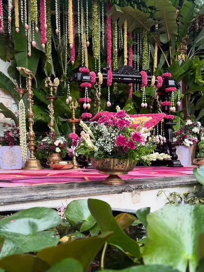A serene naming ceremony setup by the water, with a traditional cradle, hanging florals, and lily pads floating in the pond.