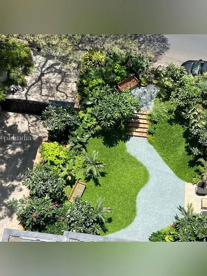 An aerial view of a South Mumbai entrance garden, showing the interplay between the curving gravel path, manicured lawn, and dense perimeter planting. The design creates a private, verdant sanctuary in a compact urban space.